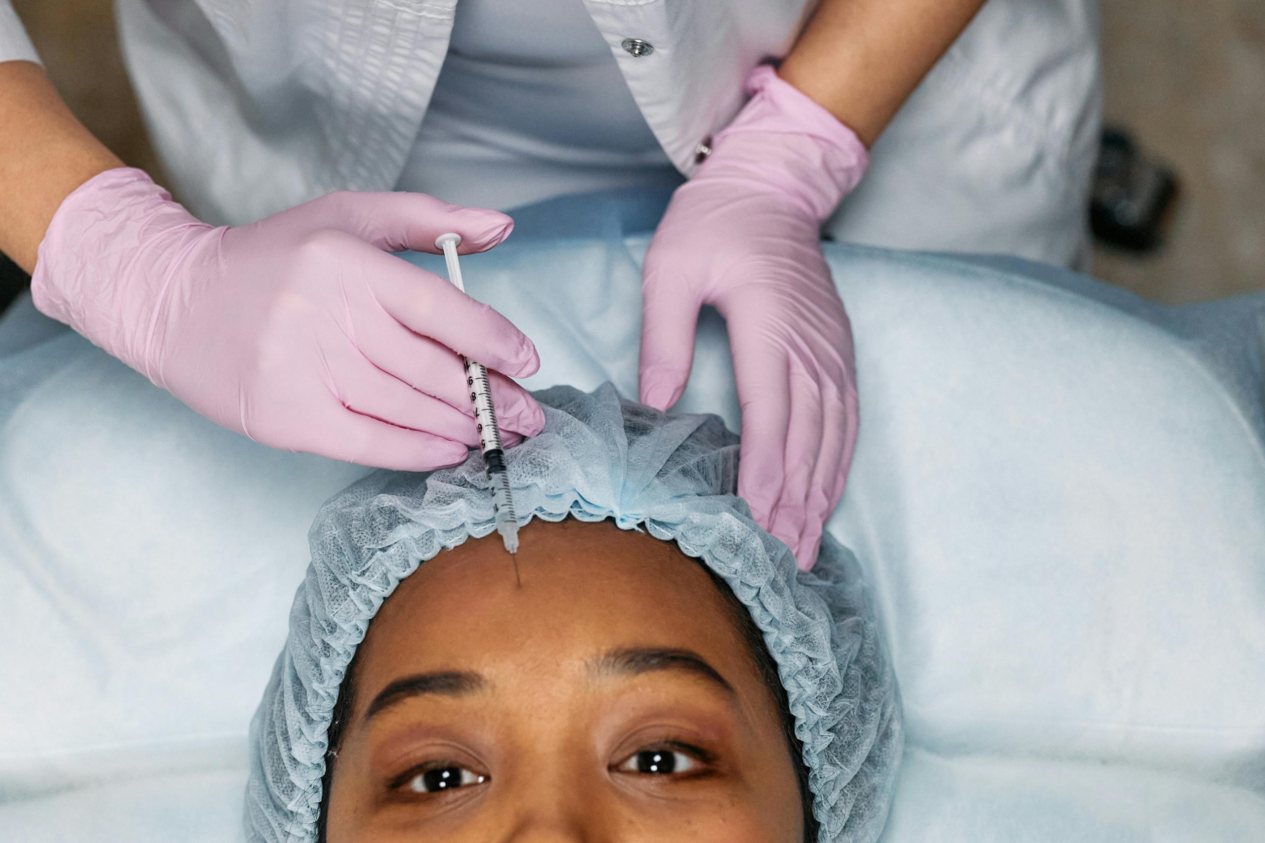 woman wearing a surgical cap receiving a Botox injection in her forehead